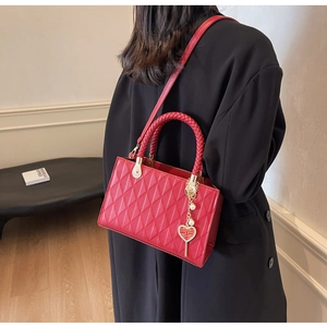 Detail of red quilted tote bag with woven handles and golden heart-shaped charm