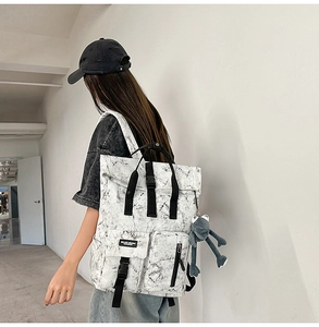 Detail of white marble backpack with thick black straps and a plush frog pendant