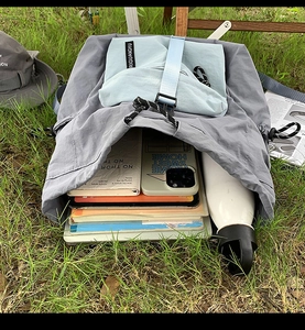 Detailed view of the backpack's interior capacity showing tablet and books on grass