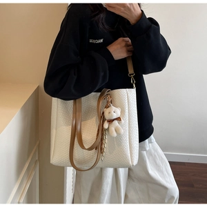 Detail of woven texture on white faux leather tote bag with brown straps and bear charm