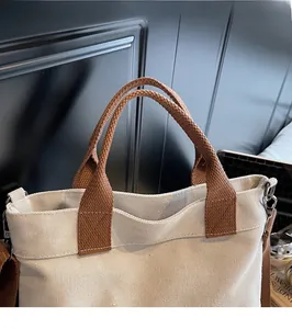 Detail of canvas tote bag showing brown woven handle and silver metal D-ring attachment