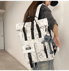 Detail view of marble print backpack with roll-top design and plush frog accessory