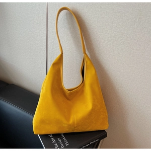 Detail of yellow hobo tote bag in suede texture placed on black books and leather chair