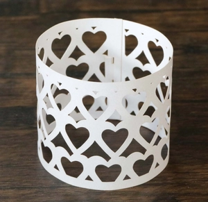 Detail of white laser-cut paper napkin ring with elegant heart-shaped hollow patterns