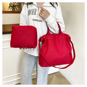 Detail view of red canvas tote bag with matching zippered pouch on casual outfit
