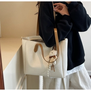 Detailed shot of large woven tote bag in cream with brown leather straps and bear charm