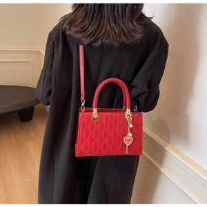 Detail of red quilted tote bag with woven handles and golden heart pearl charm decoration