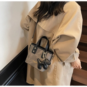 Détail du sac seau taupe avec breloque chien noir et logo de mode sur trench-coat