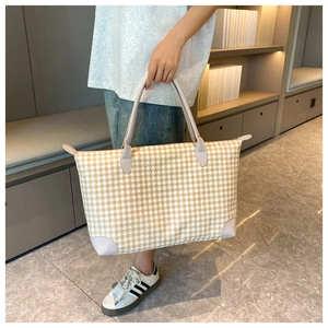 Détail d'un sac de voyage beige à motif pied-de-poule tenu par un mannequin en scène