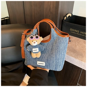 Detail of denim tote bag with brown leather handles and cute teddy bear charm accessory