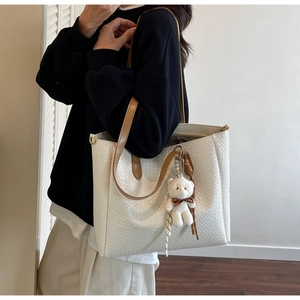 Detail of white woven tote bag with brown leather straps and plush bear charm