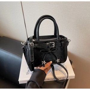 Close-up of black glossy wrinkled texture with bow and silver star detail on handbag