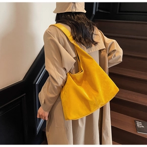 Detail of a bright yellow suede hobo tote bag held by a model in a beige trench coat
