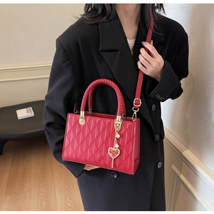 Detail of red quilted tote bag with woven handles and golden heart-shaped XI charm