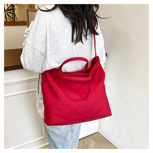 Rear view of model wearing a large red canvas tote bag with shoulder straps in a minimalist room