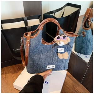 Detail of denim tote bag with brown leather trim and cute plush bear charm accessory