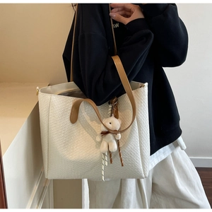 Detail view of woven texture tote bag with brown leather strap and cute bear charm