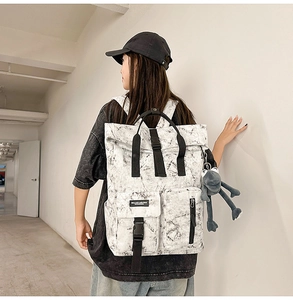 Side view of marble pattern backpack on model featuring roll-top and plush frog charm