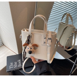 Detail of off-white lychee grain leather handbag with cute plush dog charm and straps