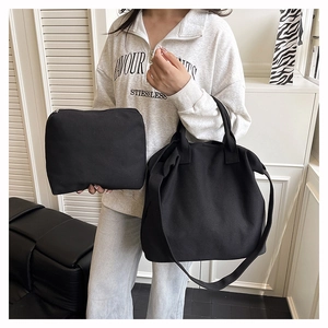 Detail view of black canvas tote bag and matching zipper pouch held by model
