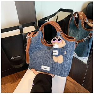 Detail of denim tote bag featuring brown leather handles and a cute bear bag charm