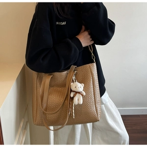 Detail of caramel woven tote bag with dual straps and a cute white teddy bear charm