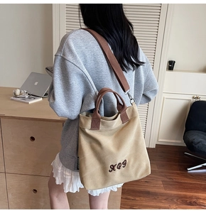 Detail of khaki canvas tote bag with brown straps and XOY embroidery in a study setting