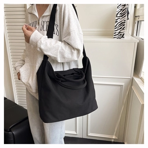 Minimalist black canvas tote bag shown on model featuring wide shoulder strap and large capacity