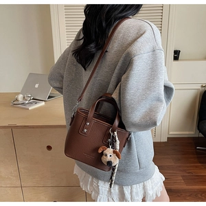 Detail of brown litchi pattern leather tote with detachable strap and plush dog charm
