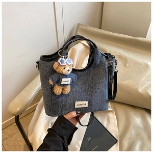 Detail of blue denim crossbody bag with black handles and cute bear charm on a seat