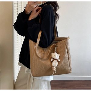 Detail of khaki woven tote bag with shoulder straps and a white plush bear charm