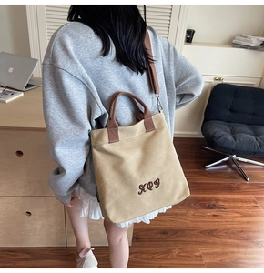 Detail of canvas tote bag with brown handles and embroidery worn by a model in casual setting