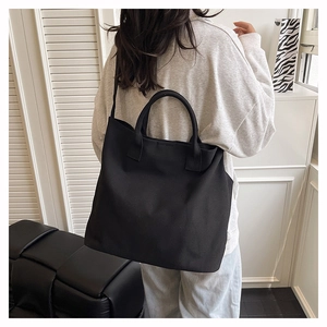 Rear view of model carrying a large black canvas tote bag for daily casual use