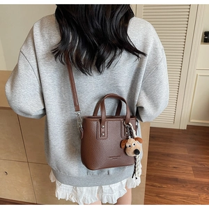 Detailed view of brown litchi pattern leather handbag with cute dog plush pendant accessory