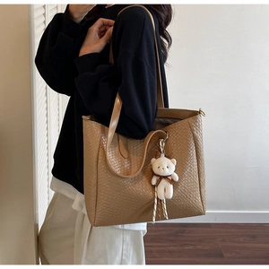 Detail of light brown woven tote bag with adjustable strap and cute teddy bear charm