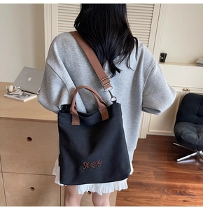 Detail of a black canvas tote with brown handles and embroidered AQG logo on the bottom