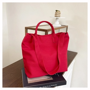 Detail of red canvas tote bag on a book with dual handles and long shoulder strap
