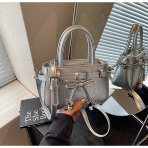 Detail of silver metallic handbag with pleated texture, ribbon bow, and star charms