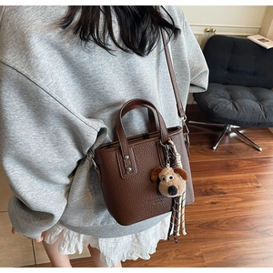 Detail of dark brown lychee leather crossbody bag with cute plush puppy charm