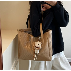 Close-up of brown woven tote bag with dual straps and a cute white bear pendant