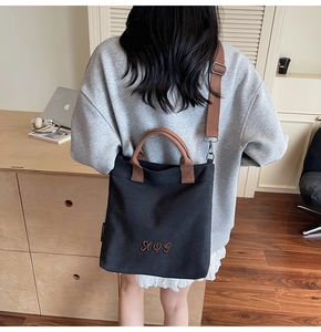 Detail of the large capacity black canvas tote bag with brown straps shown on a model