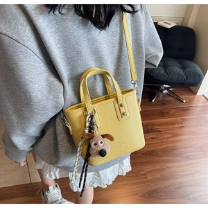 Detail of yellow lychee leather mini tote with cute puppy plush charm on model