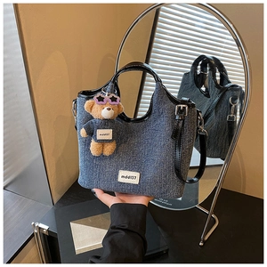 Detail of blue denim tote bag with black leather handles and plush bear charm