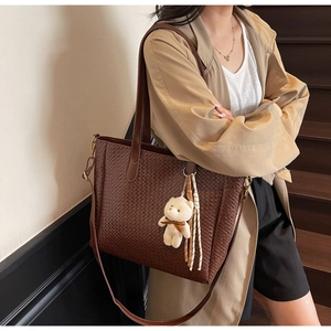 Detail of dark brown tote bag featuring intricate woven texture and plush bear charm