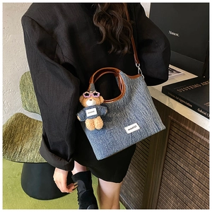 Close-up of blue denim bucket bag with brown leather trim and a cute bear keychain charm