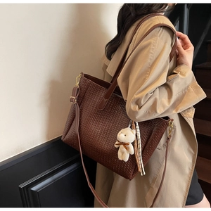 Detail of dark brown woven tote bag featuring a plush bear charm and adjustable strap