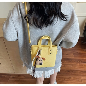 Close-up of yellow mini bucket bag featuring litchi texture and dog plush charm