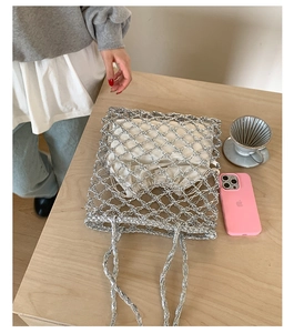 Close-up of a silver hollow-out knit tote bag featuring a white drawstring inner pouch