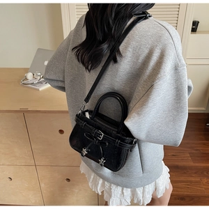 Detail of black glossy bucket bag with bow and star charms on shoulder of a model