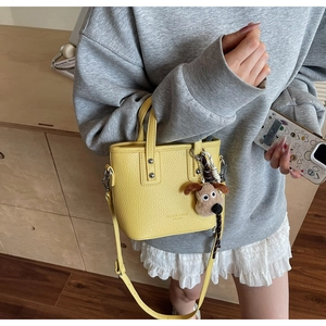 Detail of yellow lychee leather mini bucket bag with a cute brown plush puppy pendant